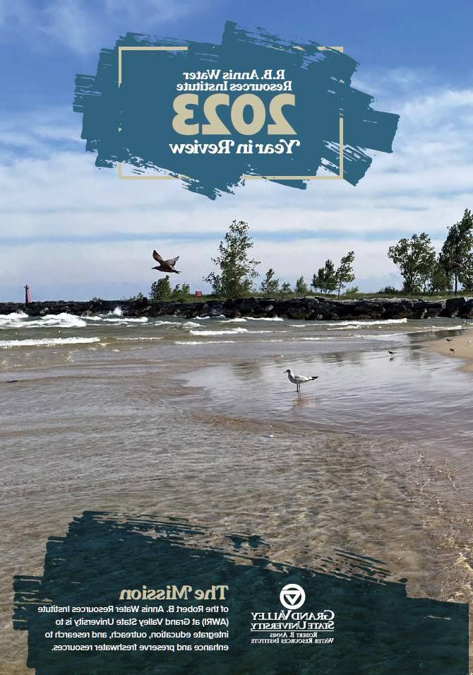 GVSU AWRI 2023 Year in Review magazine cover depicting a lakeshore scene with seagulls at a beach while trees sway from the wind. In the far distance, a red lighthouse is seen on a pier and white clouds streak across a blue sky.